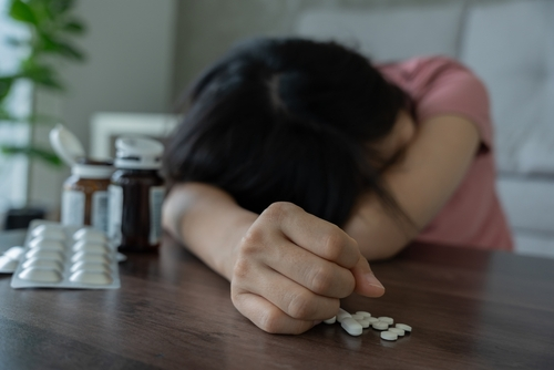 woman with her hand laying on table after taking pills