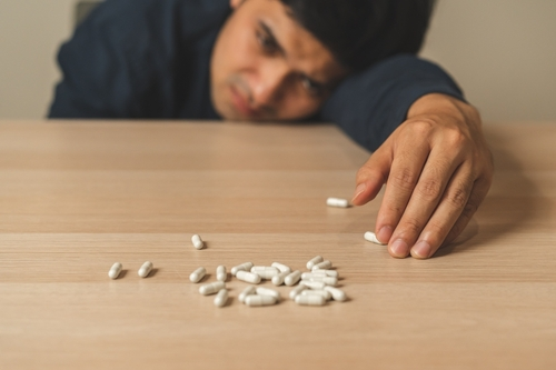 man reaching out to pills on a table looking sad