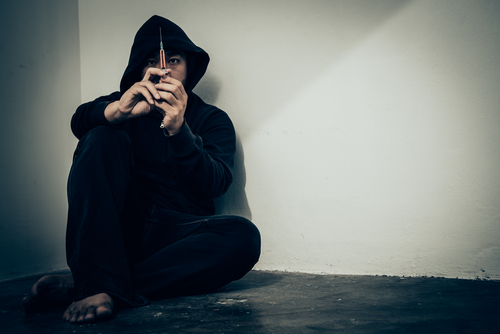 man sitting on floor holding a syringe to get high