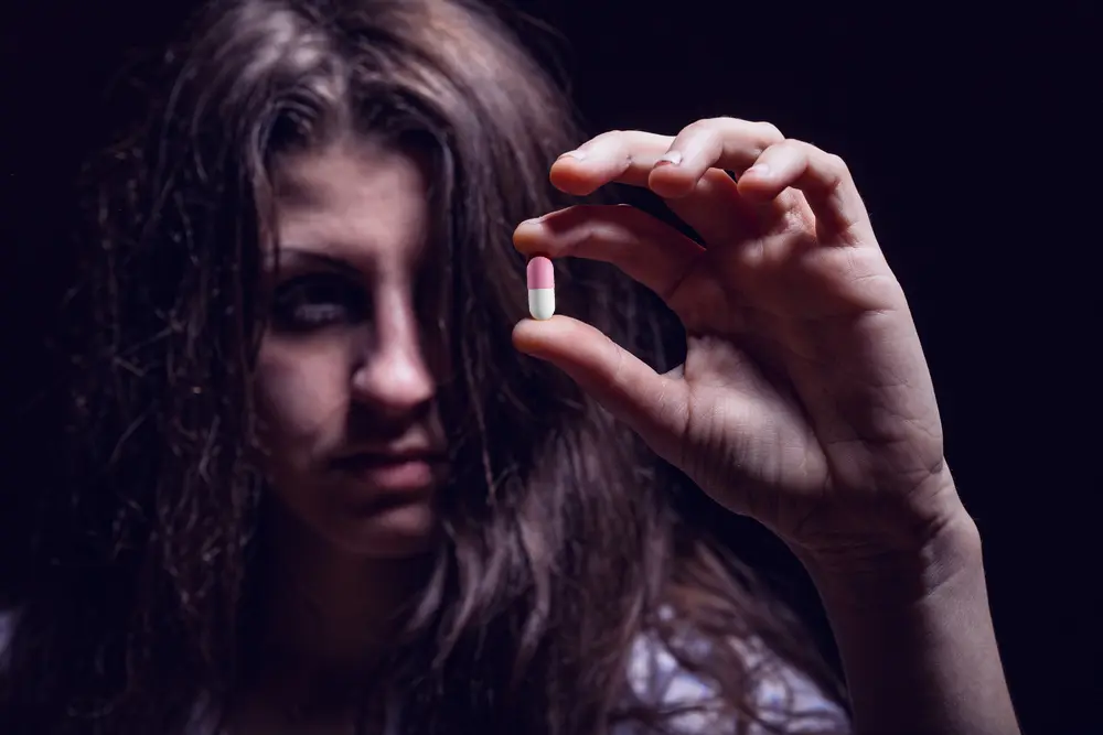 woman holding a benadryl pill while being addicted to benadryl