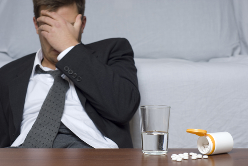 man with hand over his face with pills spilled on table and a glass of water