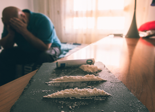 man with his head in his hand and cocaine in the foreground