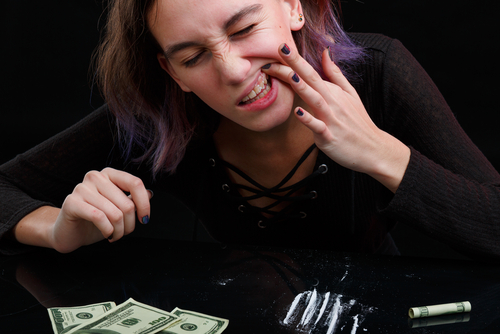 can you eat cocaine? woman rubbing cocaine on her gums with drugs around her