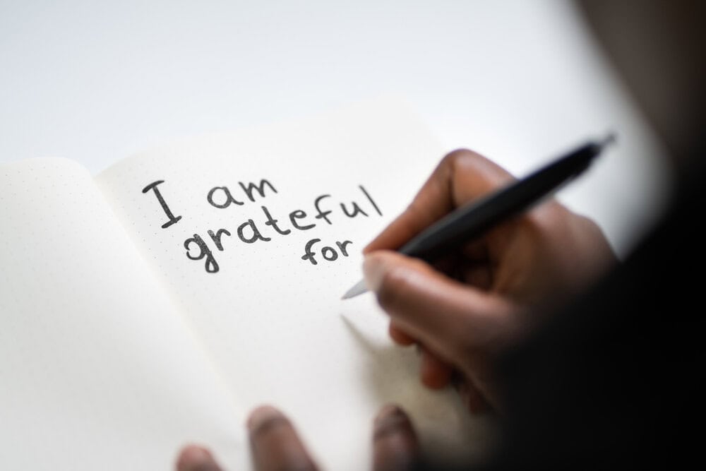 a hand holding a pen with the words "I am grateful for" on a piece of paper