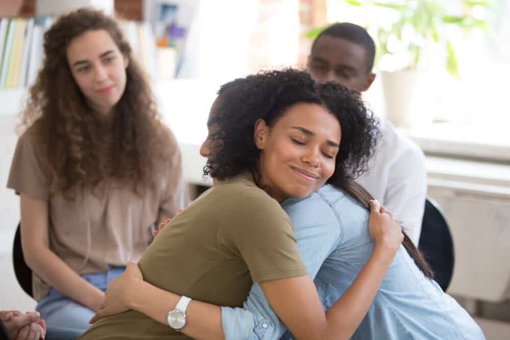 a woman hugging another woman. By helping others we are helped is one of the four paradoxes in recovery.